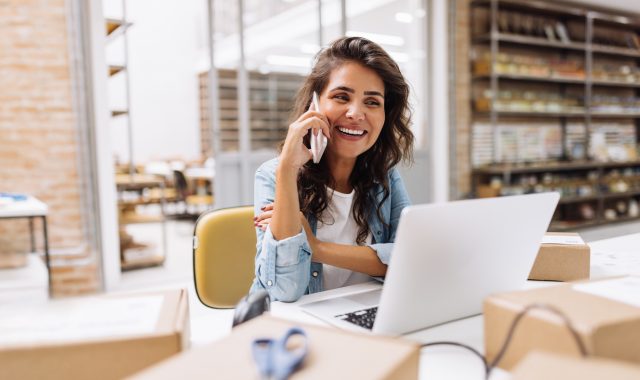 Happy young businesswoman speaking on the phone in a warehouse Werk en zekerheid